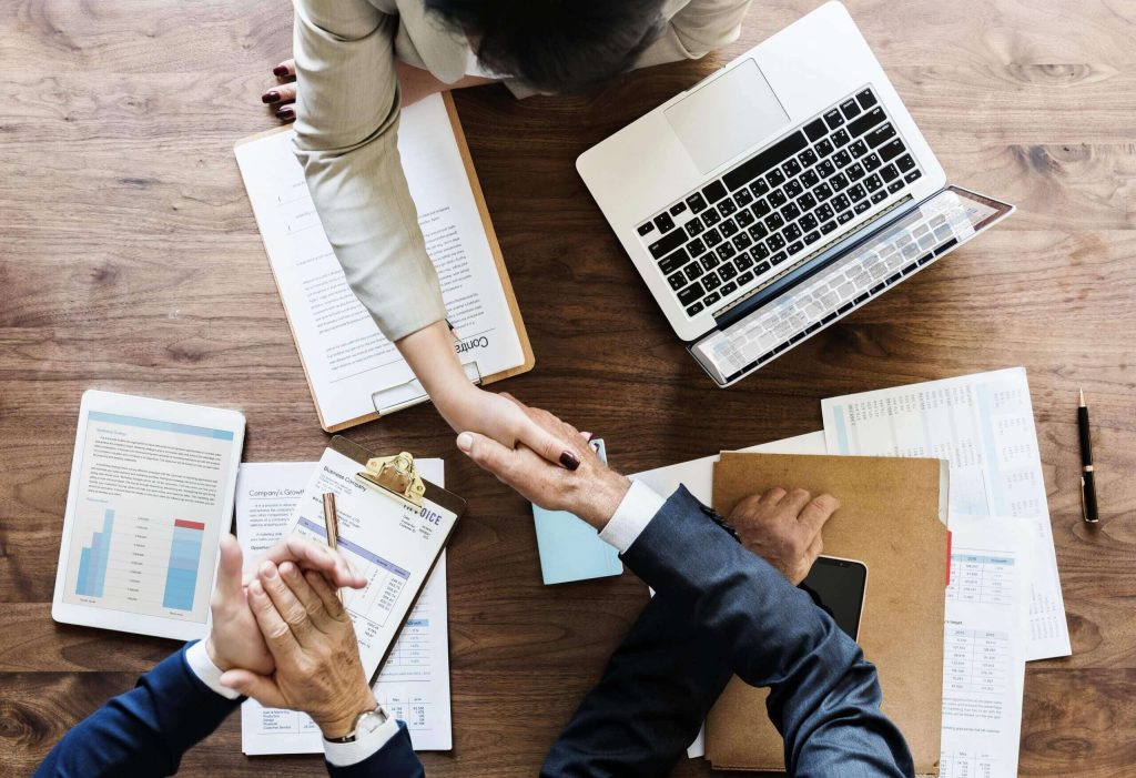 Business partners shaking hands over documents and a laptop